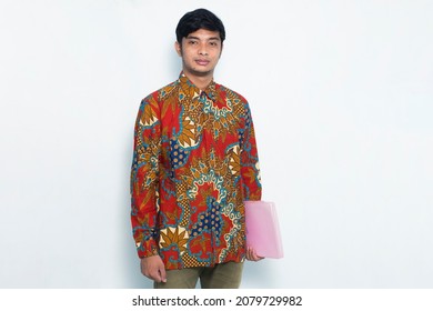 asian young man wearing batik confident while holding a pink envelope isolated on white background
