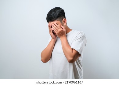 Asian young man wearing white shirt with sad expression covering face with hands while crying. depression concept over white background - Powered by Shutterstock