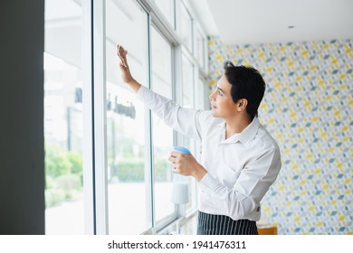 Asian Young Man White Shirt Wipe Cleaning Window Glass With Spray Alcohol For Sterilize In Restaurant. Employee Cleaning At Workplace.