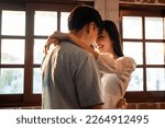 Asian young man and woman hugging each other in living room at home. Attractive romantic new marriage couple male and female spending time celebrate anniversary and valentine