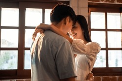 Asian Young Man And Woman Hugging Each Other In Living Room At Home. Attractive Romantic New Marriage Couple Male And Female Spending Time Celebrate Anniversary And Valentine's Day Together In House.