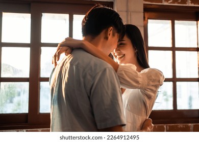 Asian young man and woman hugging each other in living room at home. Attractive romantic new marriage couple male and female spending time celebrate anniversary and valentine's day together in house. - Shutterstock ID 2264912495