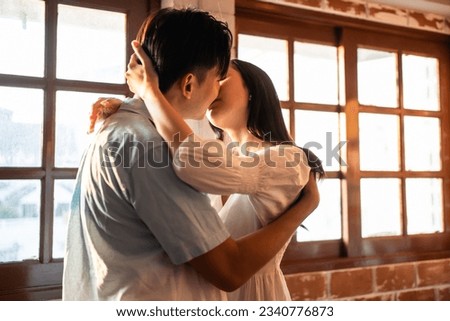 Asian young man and woman kissing each other in living room at home. Attractive romantic new marriage couple male and female spend time celebrate anniversary and valentine's day together in house.