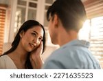 Asian young man and woman looking each other in living room at home. Attractive romantic new marriage couple male and female spend time celebrate anniversary and valentine