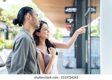 Asian Young Man And Woman Shopping Goods Outdoors In Department Store. Attractive Couple Hold Shopping Bags Then Walking Together With Happiness, Enjoy Purchasing In Shopping Mall Marketplace Center.