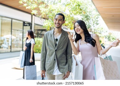 Asian Young Man And Woman Shopping Goods Outdoors In Department Store. Attractive Couple Hold Shopping Bags Then Walking Together With Happiness, Enjoy Purchasing In Shopping Mall Marketplace Center.