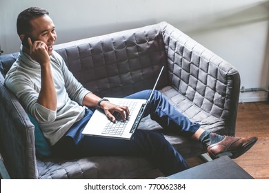 Asian Young Man Working At Home With Smartphone And Laptop On Sofa.