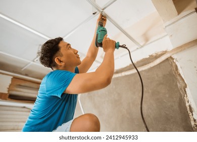 Asian young man works to install a ceiling frame with drilled bolts while renovating a roof - Powered by Shutterstock