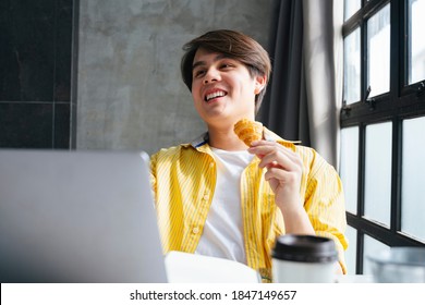 Asian young man in yellow shirt working and eating snack in modern office. - Powered by Shutterstock