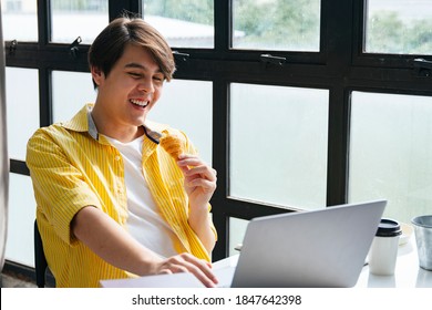 Asian young man in yellow shirt working and eating snack in modern office. - Powered by Shutterstock