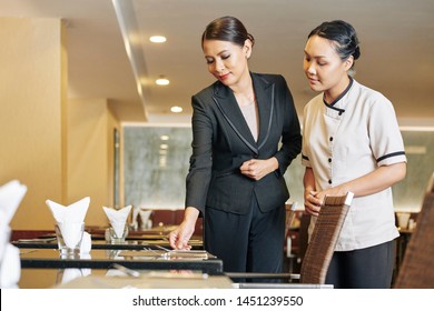 Asian Young Manager In Black Suit Showing The Process Of The Work In Restaurant To The New Waitress They Standing Near The Table And Putting The Tablewares On The Table In Order