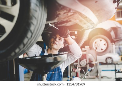 Asian Young Mechanic Working Under Car At The Garage. Mechanic Oil Change Service