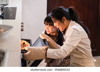 Asian young mother and daughter making pizza at home. Woman open the oven and bring the food out from machine. Little girl looking at meal and smell it with smile face, enjoy famiy activity together. - Powered by Shutterstock
