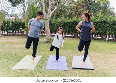 Asian Young Mother, Father And Child Daughter Practicing Exercising Stretching Together Before Yoga Workout Outdoor Morning In Nature A Field Garden Park. Happy Family Kid Sport Healthy Lifestyle