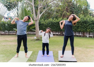 Asian Young Mother, Father And Child Daughter Practicing Exercising Stretching Together Before Yoga Workout Outdoor Morning In Nature A Field Garden Park. Happy Family Kid Sport Healthy Lifestyle