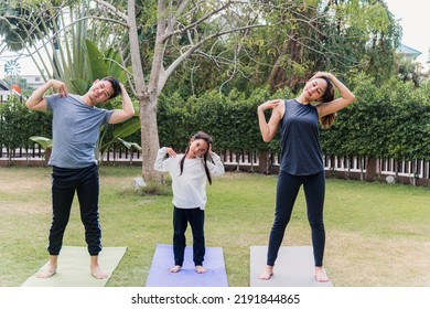 Asian Young Mother, Father And Child Daughter Practicing Exercising Stretching Together Before Yoga Workout Outdoor Morning In Nature A Field Garden Park. Happy Family Kid Sport Healthy Lifestyle