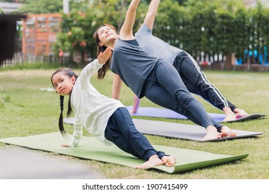 Asian Young Mother, Father Practicing Doing Yoga Exercises With Child Daughter Outdoors In Meditate Pose Together In Nature A Field Garden Park, Family Kid Sport And Exercises For Healthy Lifestyle