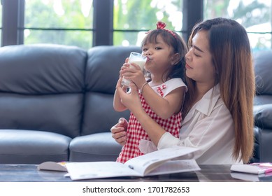 Asian Young Mother And Her Daughter Drinking The Milk. The Mom Looking The Little Girl With Happiness. Good Relationship Of Mom And Kid. Family Activity And Education Concept.