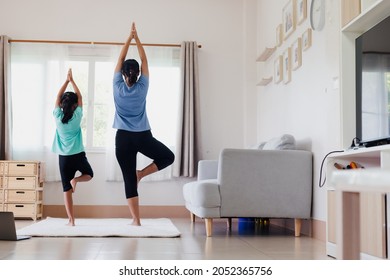 Asian young mother and her daughter doing stretching fitness exercise yoga together at home. Parent teaching child work out to be strong and maintain physical health and wellbeing in daily routine.