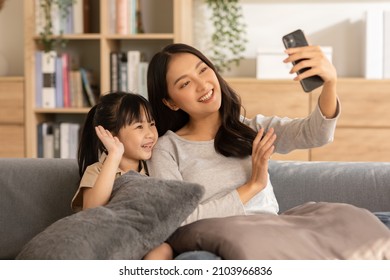 Asian Young Mother And Her Daughter Have Video Call Conference With Family Having Fun Together.Happiness Mom And Little Girl Looking At Mobile Phone And Waving Hand With Video Chat To Grandmother 