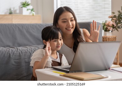 Asian Young Mother And Her Daughter Have Video Call Conference With Family Having Fun Together.Happiness Mom And Little Girl Looking At Mobile Phone And Waving Hand With Video Chat To Grandmother 