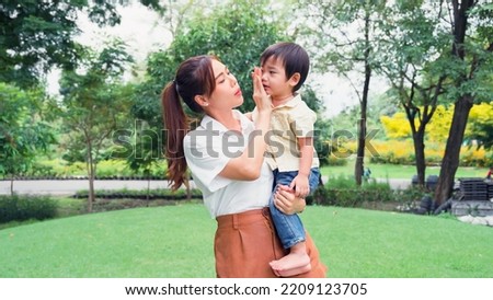 Asian young mother holding a little son of her being irritable and overbearing in park.