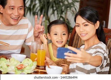 Asian Young Mother Holding Mobile Phone And Making Selfie Portrait Of Her Family While They Having Dinner At The Table