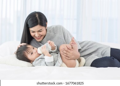 Asian young mother See also baby and asian baby suck  milk from bottle and sleep on white bed
