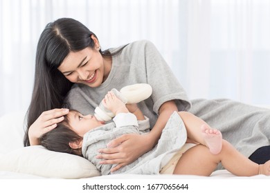 Asian young mother See also baby and asian baby suck  milk from bottle and sleep on white bed