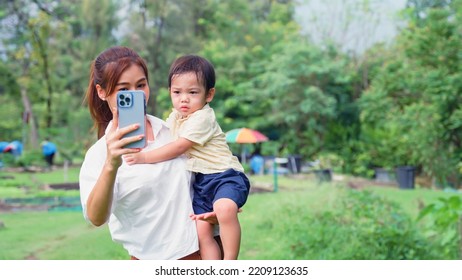 Asian Young Mother Taking A Selfie With A Cute Little Son Her In The Park While Her Son Was Irritated And Overbearing.