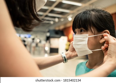 Asian Young Mother Wearing Face Mask For Little Kid Before Going Shopping In Department Store For Prevent Covid 19 Infection During Virus Pandemic. The Child Looking At Mom When Taking Care Of Her.