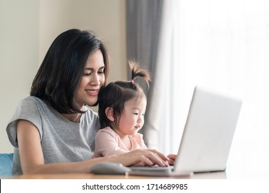 Asian young mother work from home. Woman use laptop for meeting with colleague while baby girl sit on the lap and smile. Mom happy to do job while taking care family. Covid19 Social distancing concept - Powered by Shutterstock