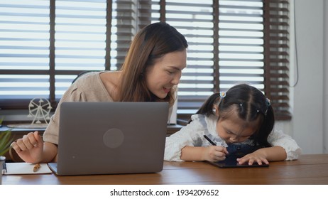 Asian Young Mother Working With Laptop Computer At Home And Help Daughter Doing Homework, Single Mom Freelancer Work From Home And Helping His Girl Kid Teaching Homework On Desk