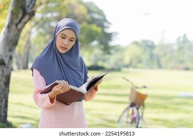 Asian young Muslim woman wear hijab headscarf and hijab dress standing and reading a book in the park
