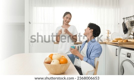 Asian young newlywed couple smile and drinking espresso coffee and hot milk tea in a mug on a kitchen table while morning talk about planning pregnant and having a baby after eating breakfast together
