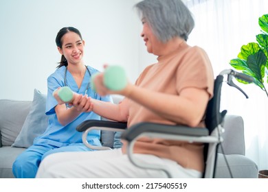 Asian Young Nurse Help And Support Elderly Or Senior Woman To Exercise With Dumpbell In Living Room With Day Light And They Look Happy With This Activity Together. 