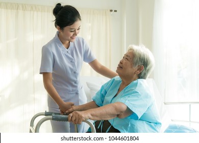 Asian young nurse supporting elderly patient disabled woman in using walker in hospital. Elderly patient care and health lifestyle, medical concept.
