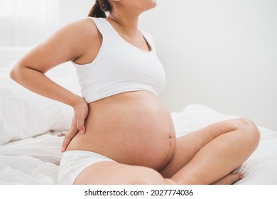 Asian young pregnant woman with big belly has backache, back pain on bed