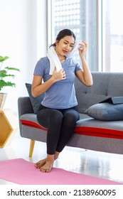 Asian Young Pretty Happy Healthy Female Athlete Sport Girl In Casual Sporty Outfit Sitting Smiling On Sofa Holding Using White Towel Cleaning Drying Sweat Relaxing Resting After Exercising Online.