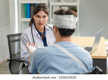 Asian Young Professional Female Practitioner Doctor In White Lab Coat With Stethoscope Holding Skull Model Showing Explaining To Unrecognizable Male Patient Sitting On Wheelchair After Brain Surgery.