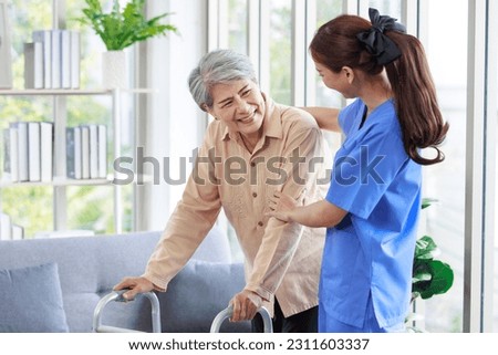 Asian young professional successful friendly female nurse in blue hospital uniform helping supporting physical therapy senior old pensioner unhealthy injury woman patient walking via four legs walker.