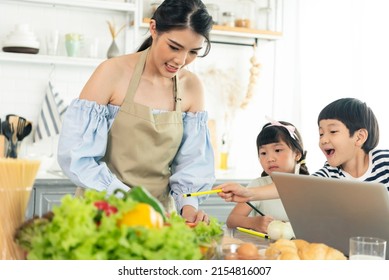 Asian Young Single Mother Making Food While Taking Care Child In Kitchen. Home School And Single Mother Concept.