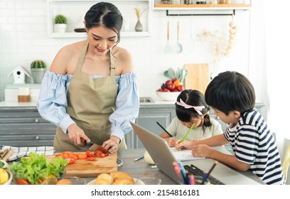 Asian Young Single Mother Making Food While Taking Care Child In Kitchen. Home School And Single Mother Concept.