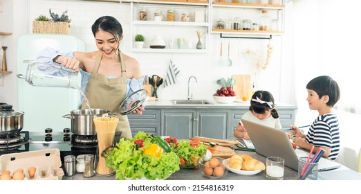 Asian Young Single Mother Making Food While Taking Care Child In Kitchen. Home School And Single Mother Concept.