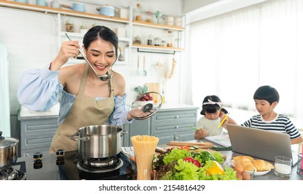 Asian Young Single Mother Making Food While Taking Care Child In Kitchen. Home School And Single Mother Concept.