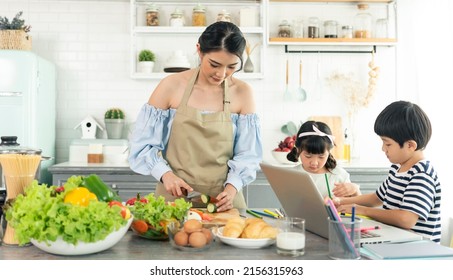 Asian Young Single Mother Making Food While Taking Care Child In Kitchen. Home School And Single Mother Concept.