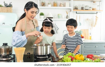 Asian Young Single Mother Making Food While Taking Care Child In Kitchen. Home School And Single Mother Concept.