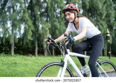 Asian young sport woman riding bicycle in the evening in public park. Beautiful athlete fit and firm girl in sportswear wear helmet, exercise by cycling workout for her health care wellness and fresh. - Powered by Shutterstock