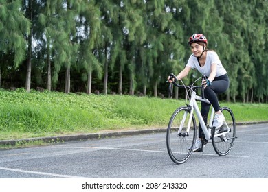 Asian young sport woman riding bicycle in the evening in public park. Beautiful athlete fit and firm girl in sportswear wear helmet, exercise by cycling workout for her health care wellness and fresh. - Powered by Shutterstock