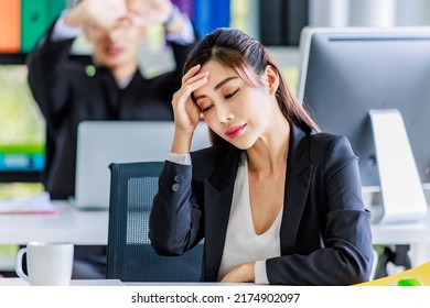 Asian young stressed depressed tired exhausted female businesswoman employee staff in formal suit sitting holding hands at head having problem migraine headache same as businessman colleague behind. - Shutterstock ID 2174902097